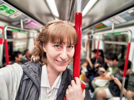 A middle-aged woman takes a selfie while riding the subway, sharing her travel experience and capturing the urban atmosphere.