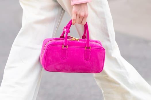 Paris, France - March 11, 2025: Woman wears structured suede handbag in bright pink with gold zipper detail. Minimalist luxury fashion accessory in street style. Modern outfit look.