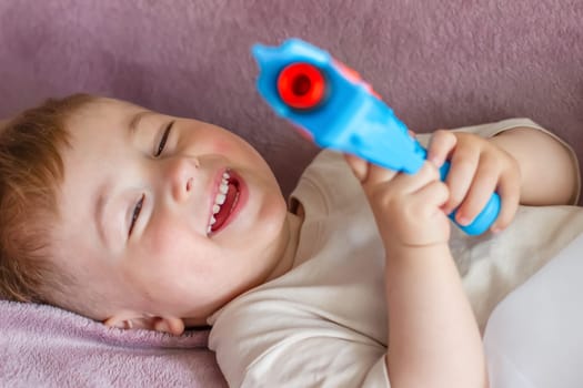 A child lies down and laughs with a toy gun in his hands. High quality photo