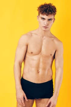 Stylish young male model with defined physique and curly hair stands confidently on a vivid yellow background. Personal branding, fitness, and healthy lifestyle concept.