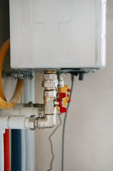 Close-up view of water heater pipes and valves in a utility room, featuring colorful connectors and tubes. Essential components for heating system maintenance and operation. Gas boiler taps.