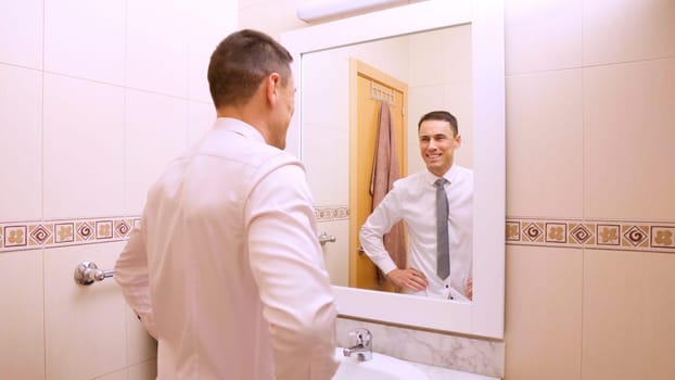 Businessman getting ready for work, smiling at his reflection in the bathroom mirror, feeling confident and successful