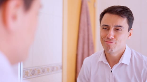 Happy businessman wearing a white shirt looking and smiling at his reflection in a bathroom mirror