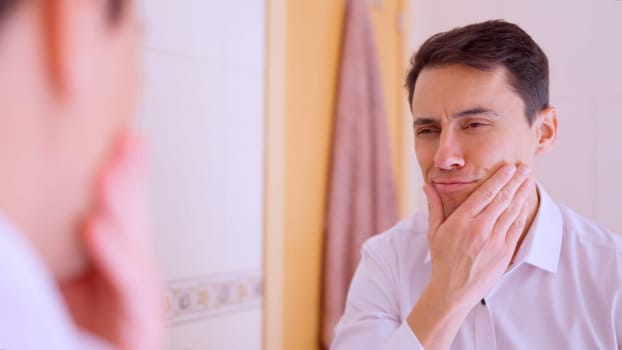 Businessman touching his face and looking in the mirror in the bathroom