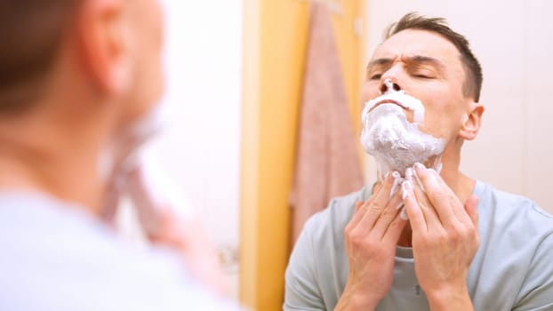 Man applying shaving cream getting ready to shave his beard in bathroom mirror