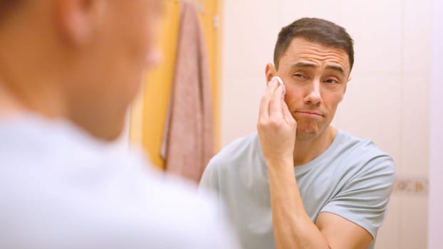 Caucasian man using cotton pad for cleaning face skin after shaving in bathroom
