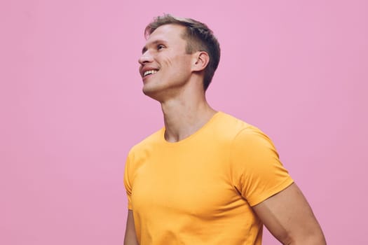 smiling man wearing yellow t-shirt looking side up with cheerful expression isolated on pink background casual style positive emotion digital nomad concept illustrating remote work lifestyle and freedom