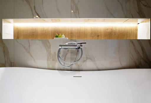 A modern chrome faucet with hose above freestanding bathtub in elegant bathroom interior.