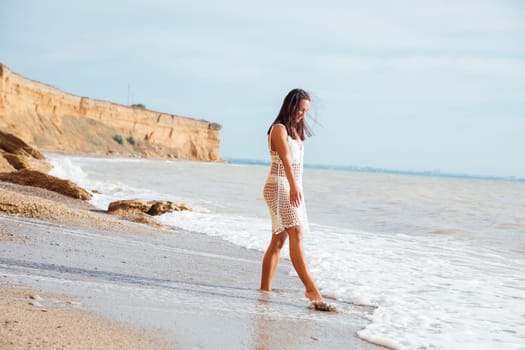 Brunette in a light dress walking on a sandy sea beach