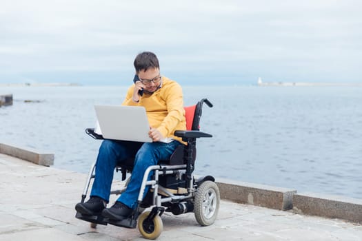 A man in a wheelchair came to the sea to work online on a laptop for business