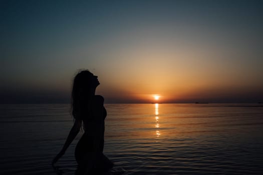 Silhouette of slender woman on the beach at sunset by the sea