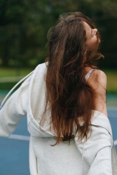 Carefree young woman with long hair, dressed in a grey hoodie, smiling and enjoying the outdoors during summer Captures a joyful, relaxed emotion with vibrant green background