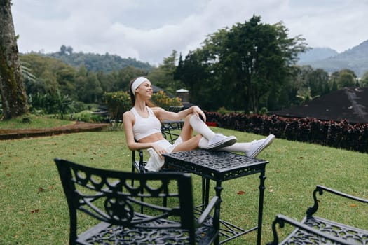 A young woman in sporty attire smiles while relaxing in a garden The scene embodies fitness, tranquility, and healthy living in nature