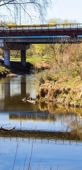 Yellow bus crossing the bridge, casting reflection in the water