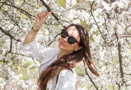 Beautiful woman poses for photo in the blooming with flowers garden