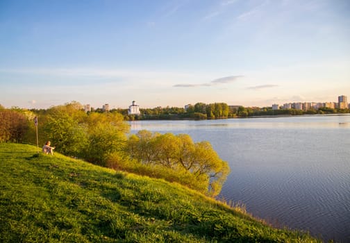 Minsk, Belarus - 05.04.2025 - Sun is setting by the lake with city buildings on the background