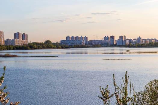 Sun is setting by the lake with city buildings on the background