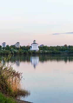 Sun is setting by the lake with city buildings and church on the background