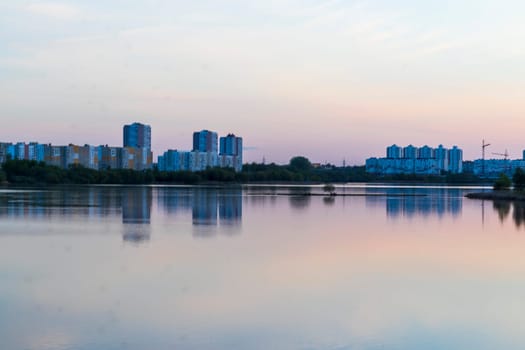 Sun is setting by the lake with city buildings on the background
