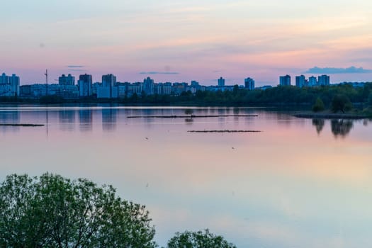 Sun is setting by the lake with city buildings on the background