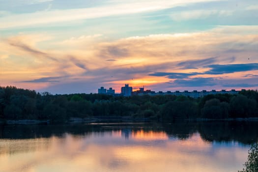 Sun is setting by the lake with city buildings on the background