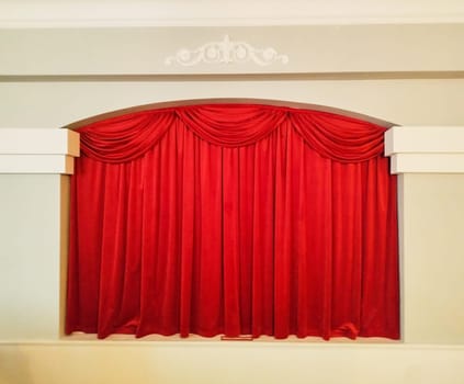 A rich red curtain hangs elegantly in a theater setting, beautifully framing the stage. The fabric is smooth and drapes in soft folds, creating a luxurious atmosphere.