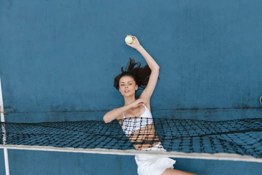 Energetic female athlete serving a tennis ball in stylish white activewear, set against a vibrant blue backdrop, perfect for sports, fitness, and healthy lifestyle themes