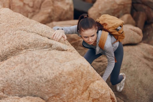 Woman in activewear climbing on rocky terrain, displaying excitement and determination Ideal for adventure, fitness, and outdoor activity themes, capturing the spirit of exploration