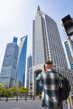 A male tourist in a casual shirt and backpack takes a smartphone photo of Shanghai’s futuristic skyline, showcasing travel blogging and social media moments in urban Asia.
