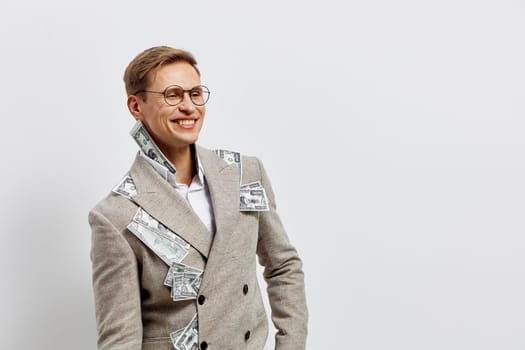 Smiling young caucasian man in stylish beige coat with money bills tucked in pockets and collar, looking confident and happy, symbolizing financial success, wealth, and digital nomad lifestyle concept on plain light background