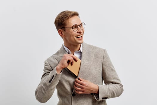Happy smiling man with glasses dressed in a gray blazer holding a notebook, standing against a plain background. Genuine expression of confidence and positivity, ideal for business or education themes, modern professional look.
