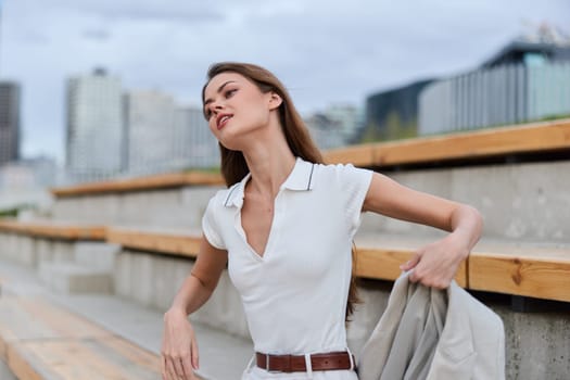 Confident young woman in white shirt with beige jacket outdoors, urban background, casual fashion style, summer season, natural light, lifestyle concept
