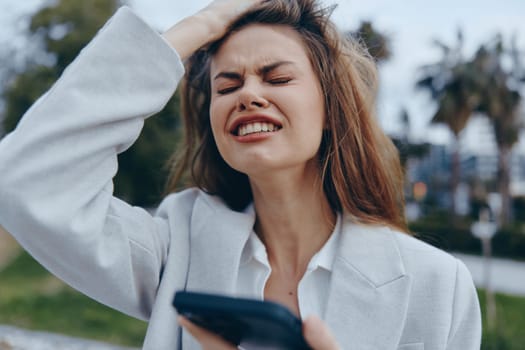 A businesswoman expressing frustration outdoors, wearing a stylish suit while holding a smartphone. The image captures the pressures of modern work life with a seasonally appropriate setting.