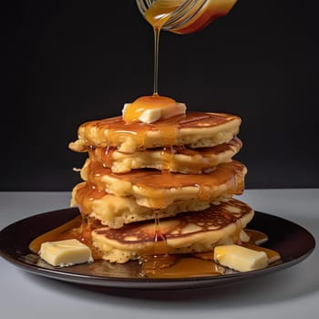 Pancakes with butter, honey and maple syrup on a black background