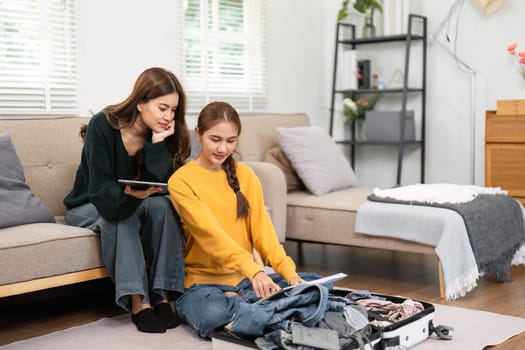 Two young women discussing travel plans while packing a suitcase, showcasing excitement and friendship.