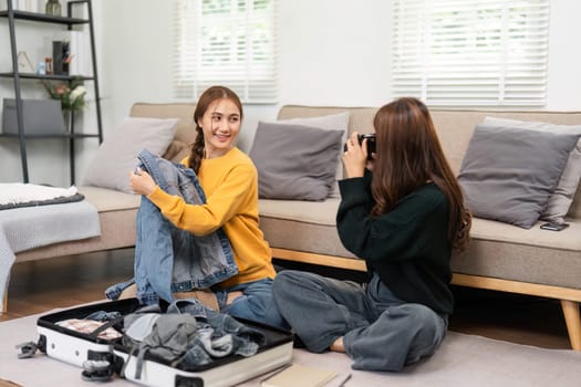 Two young women packing clothing into a suitcase while enjoying photography at home, illustrating friendship, preparation, and creativity.