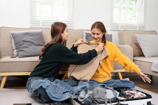 Two friends happily preparing outfits and clothes together on the floor, showcasing friendship and teamwork in a light-filled living space.