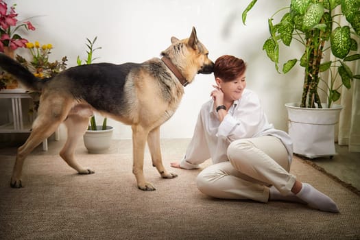 Middle-aged woman sits on the floor with her German Shepherd in a cozy room, enjoying a relaxed moment.