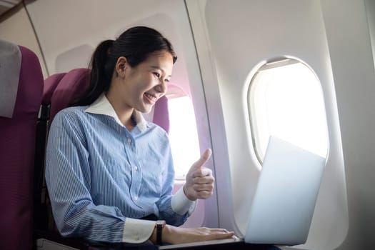 A young professional engaging in productive work on her laptop while flying, smiling with joy and satisfaction amidst the travel environment.