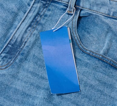 Close-up of light blue denim jeans with a blank blue price tag attached to the belt loop. Visible pocket and seams