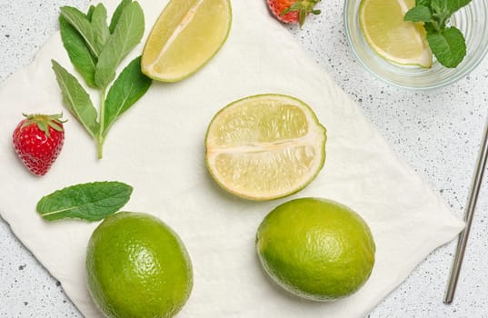 A top down view of ingredients for a refreshing drink, including whole and sliced limes, fresh mint sprigs, empty glass, metal straw