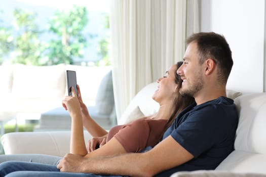 Happy couple using smart phone sitting on a couch in a luxury house