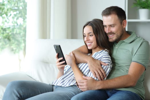 Happy couple using mobile phone together sitting ona couch at home
