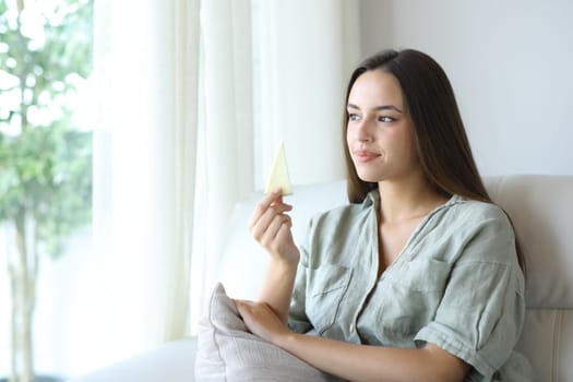 Woman holding a piece of cheese sitting on a couch at home