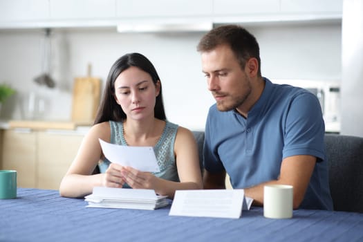 Serious interracial couple reading bank letter in the kitchen at home
