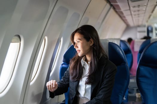 A young businesswoman gazes thoughtfully out the window of an airplane, contemplating her journey during a flight.