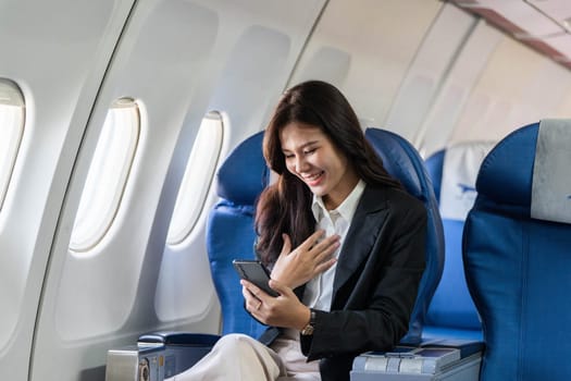 A young professional woman engages with her smartphone while traveling on an airplane, showcasing the blend of business and travel.
