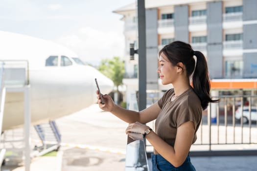 A young woman checks her phone while gazing ahead at the airport, embodying the anticipation of an upcoming flight.