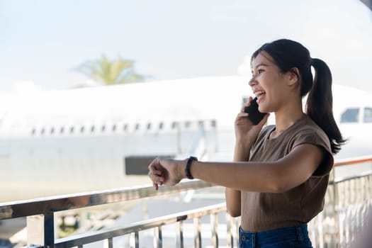 A young woman happily chatting on her phone at the airport, showcasing the blend of travel excitement and professional life.
