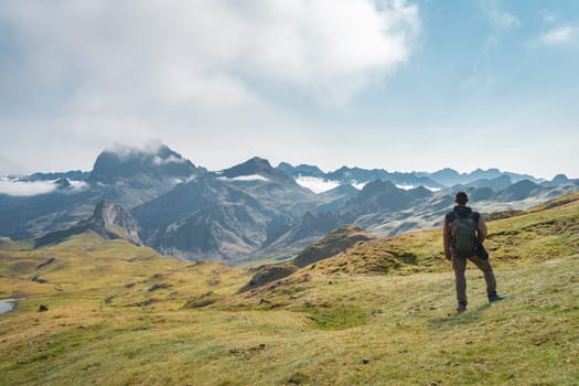 A lone explorer stands still, gazing in awe upon the breathtaking mountain scenery beneath a bright blue sky